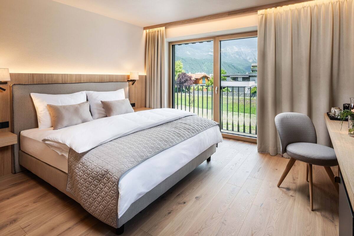 Une chambre d’hôtel moderne, dotée d’un grand lit, d’un bureau et offrant une vue sur un paysage montagneux par la fenêtre.