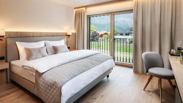 Ein modernes Hotelzimmer mit einem großen Bett, einem Schreibtisch und Blick auf eine Berglandschaft durch das Fenster.