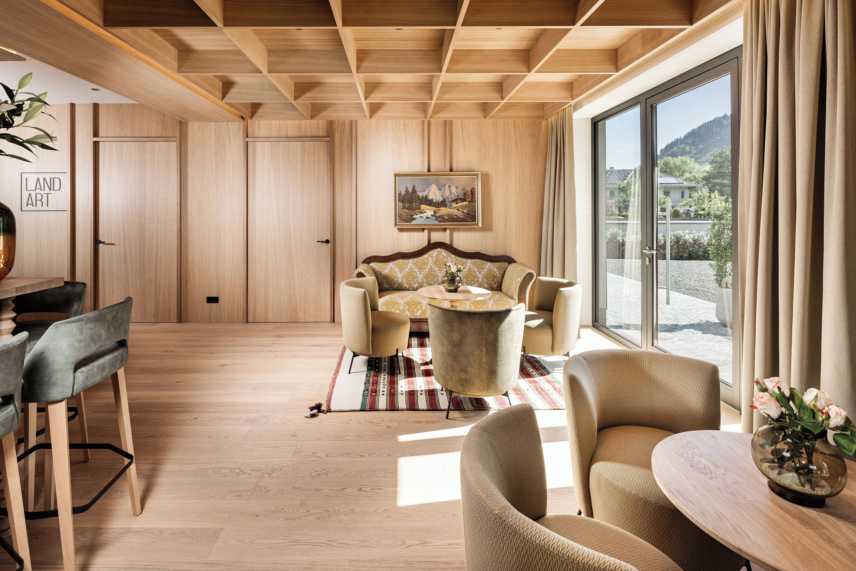 Un interior moderno con paneles de madera, una zona de comedor con sillas y una mesa, y un ventanal con vistas a montañas.