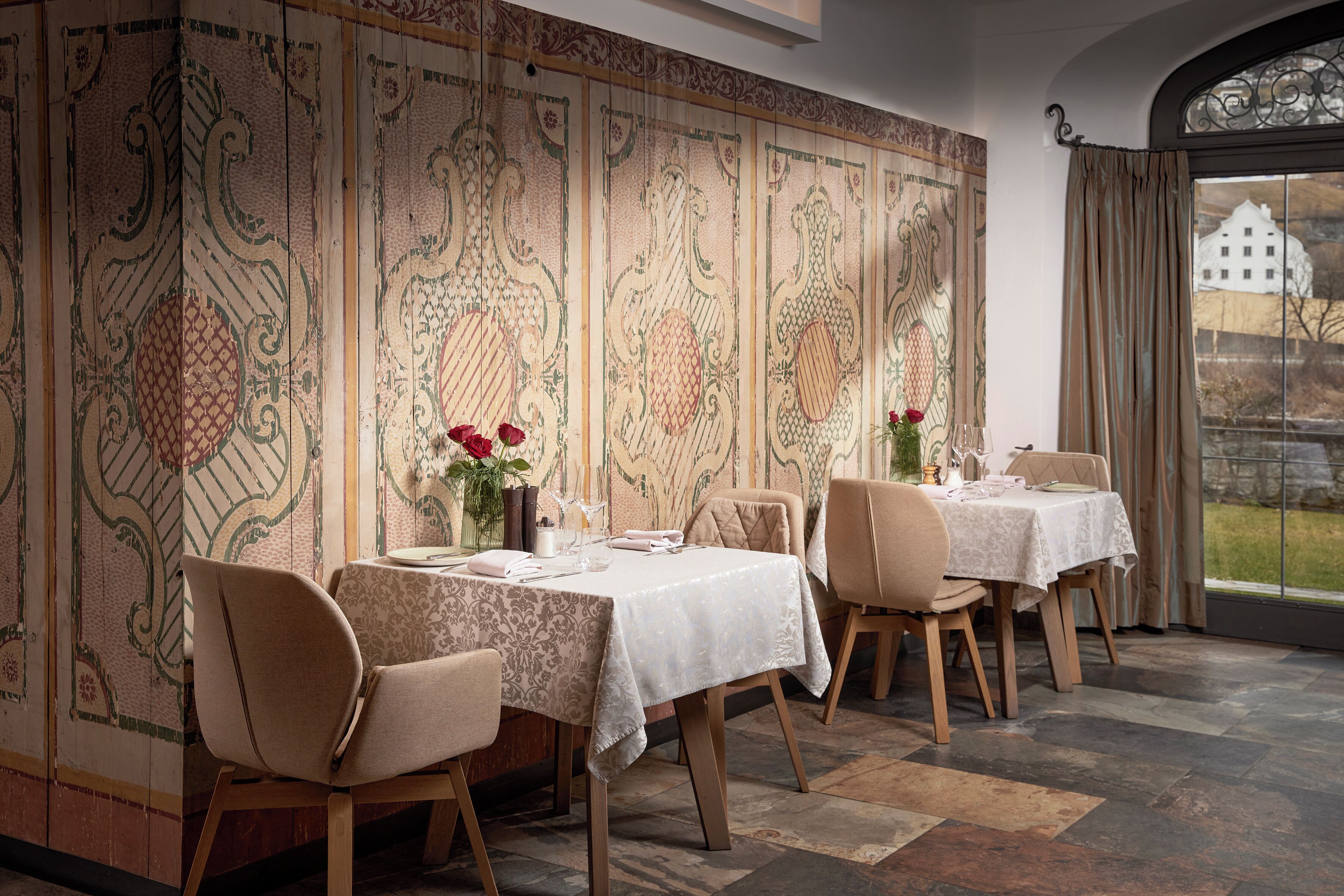 A dining area with a high ceiling, patterned wallpaper, and a view of a building through a window.