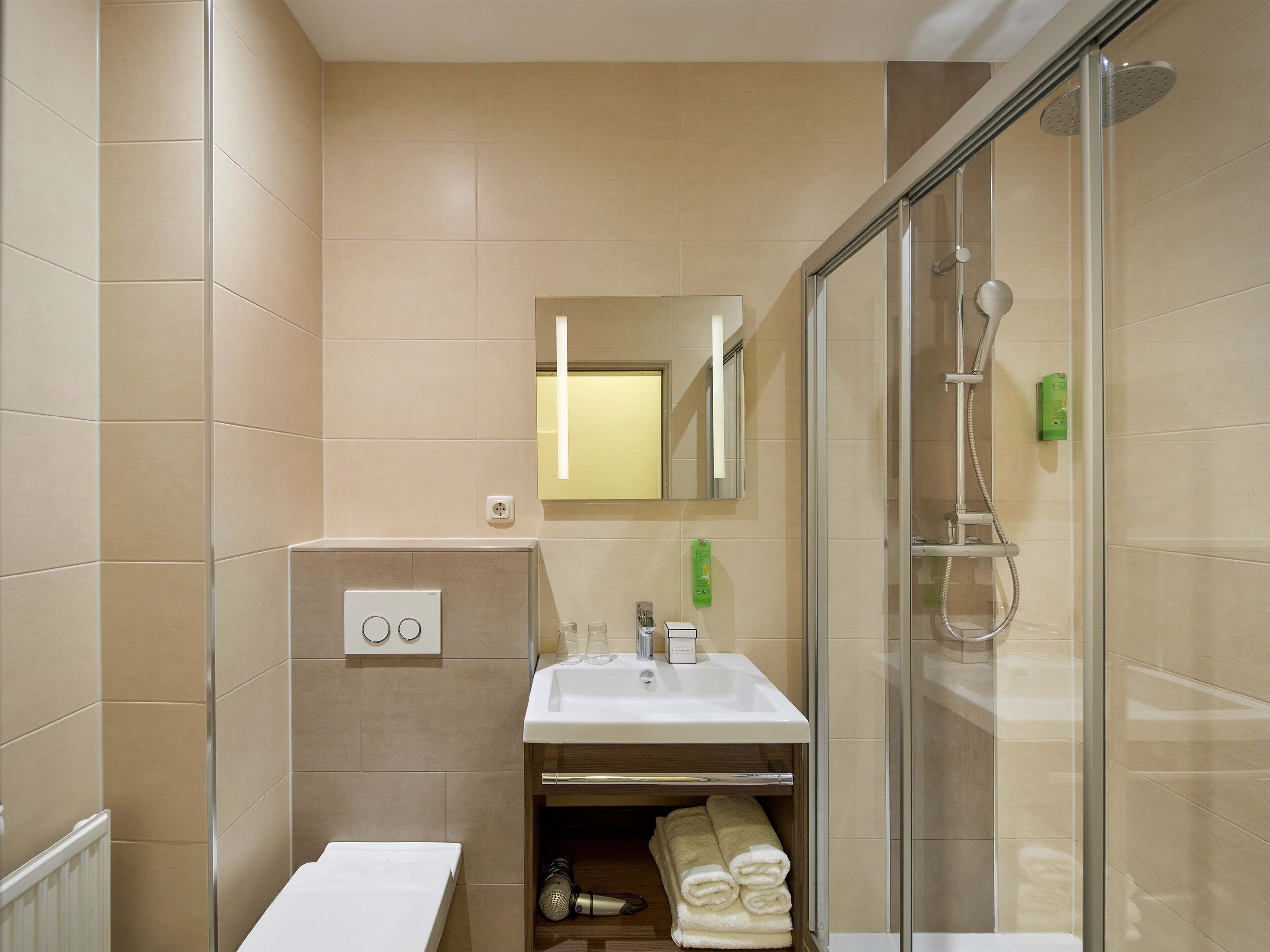 A bathroom with a glass-enclosed shower, a sink with a mirror above it, and a towel rack with towels.