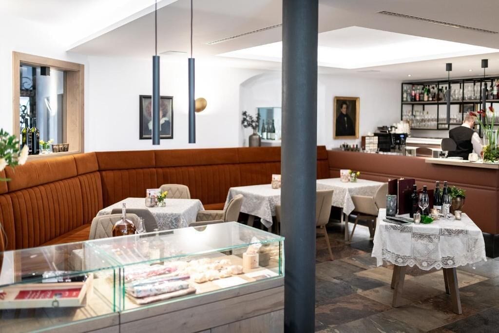 A modern restaurant interior with a central seating area, tables with white lace tablecloths, and a glass display case with food items.