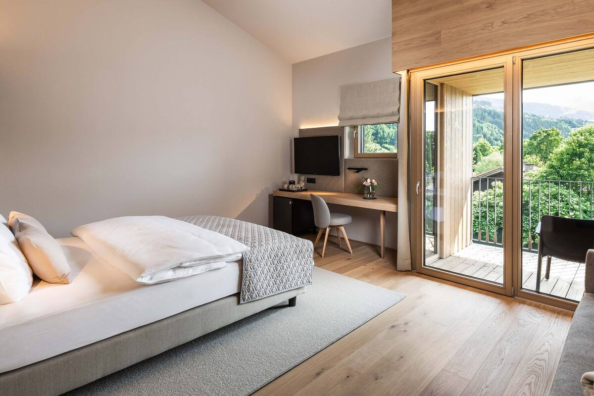 Une chambre moderne équipée d’un lit, d’un bureau et d’une grande fenêtre donnant sur l’extérieur.