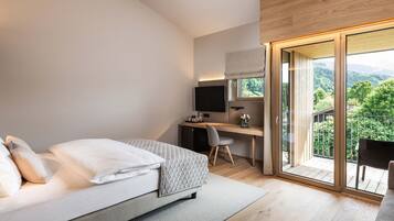 A modern bedroom with a bed, a desk, and a large window offering a view of the outdoors.