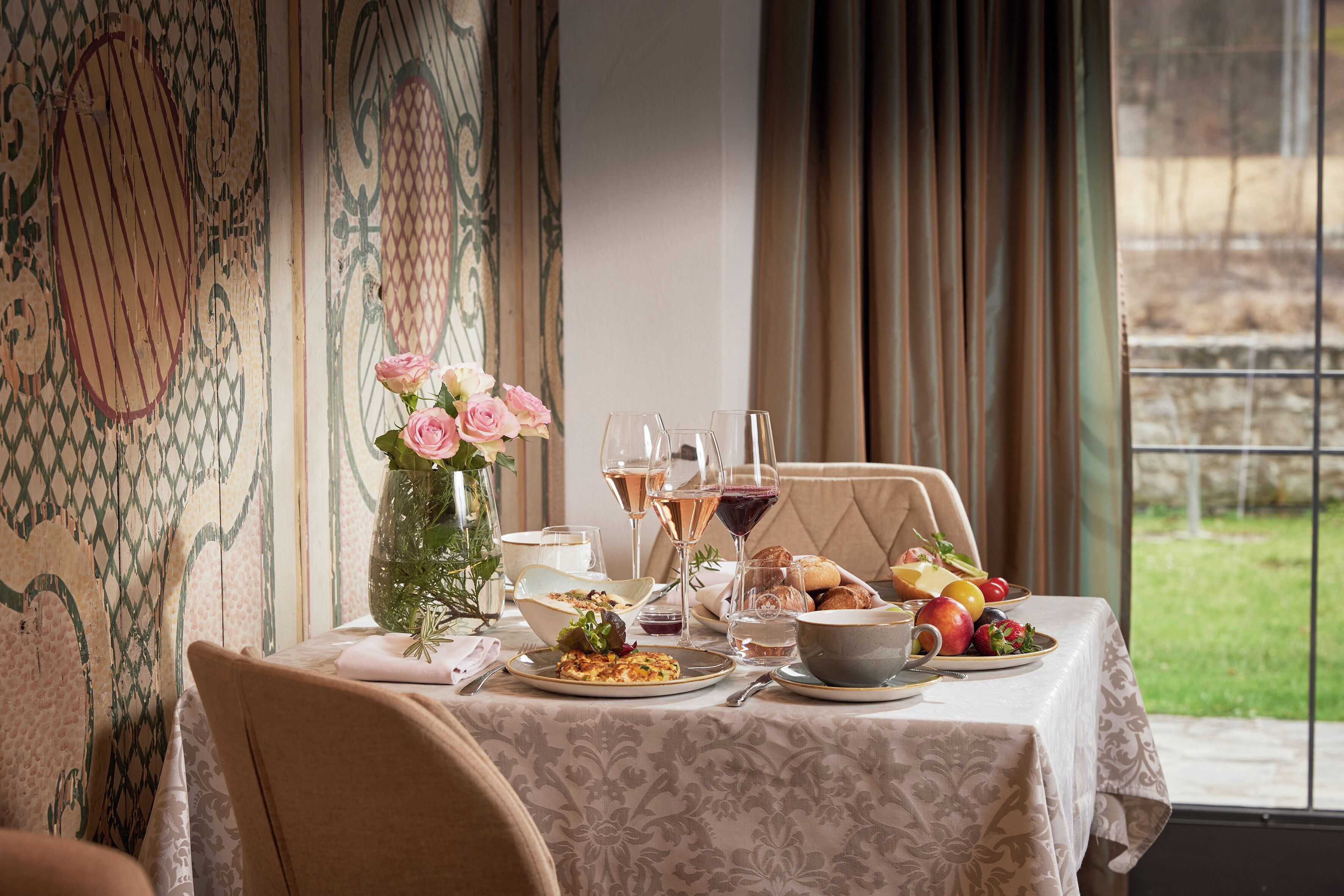 A dining table with a floral centerpiece, wine glasses, and a fruit bowl.