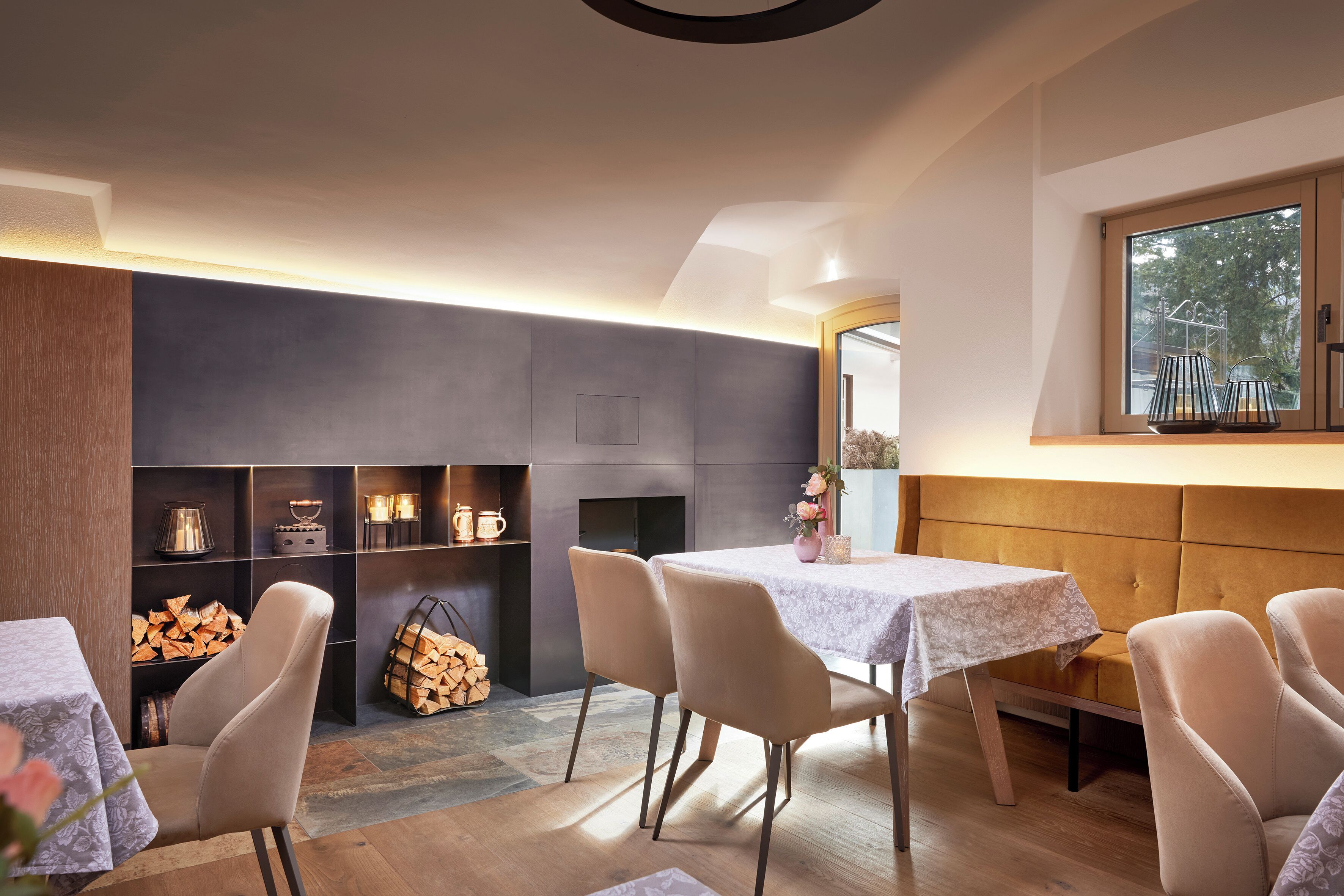 A modern dining area with a fireplace, wooden shelves, and a large window.