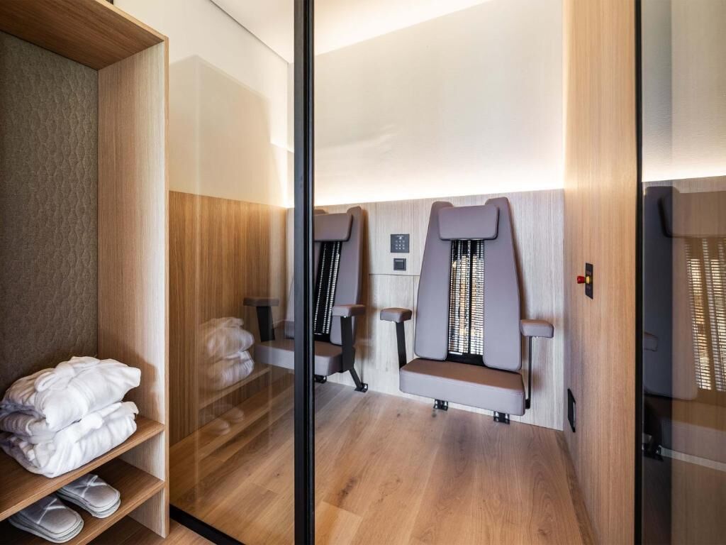 A modern spa room with wooden flooring, a glass partition, and two massage chairs.