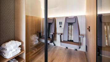 A modern spa room with wooden flooring, a glass partition, and two massage chairs.