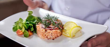 Ein weißer Teller mit Lachstartar, einem Beilagensalat und Zitronenscheiben.