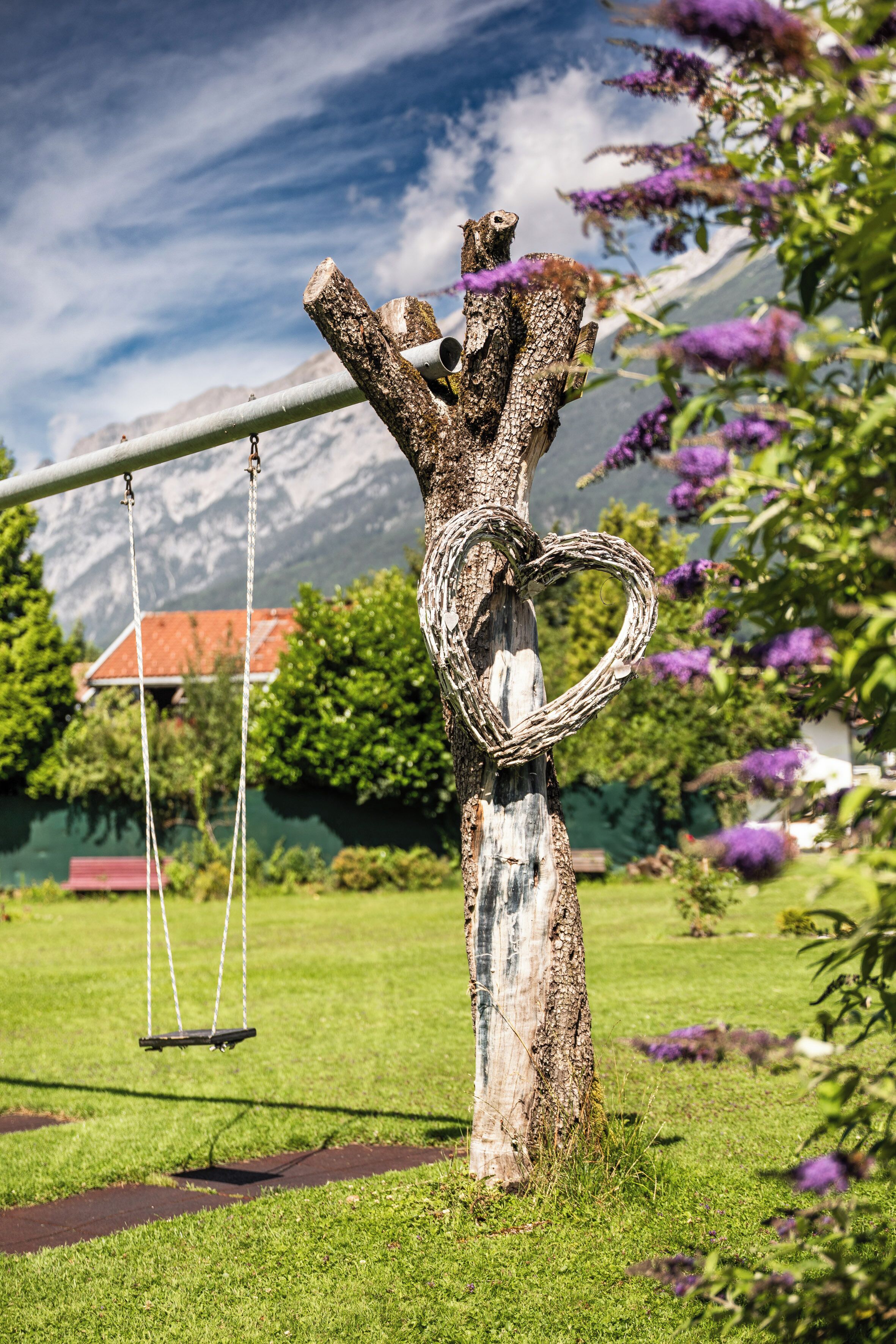Ein Baum mit Herz-Dekoration, einer Schaukel und einem Berg im Hintergrund.