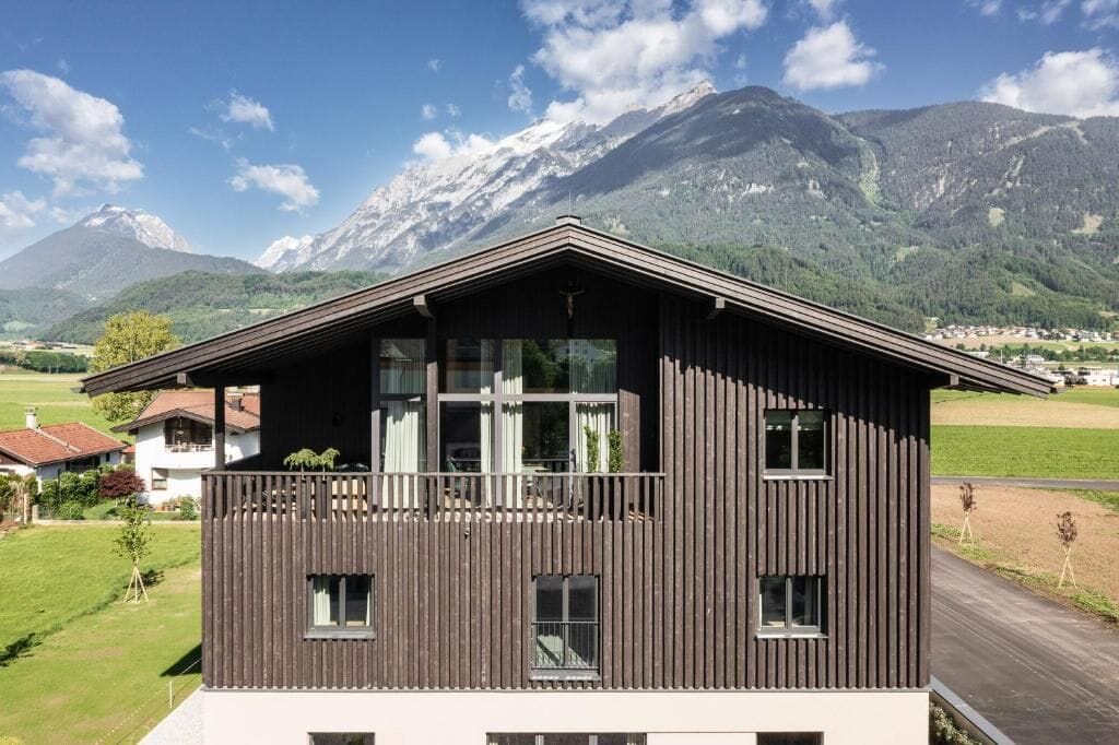 A modern two-story building with a balcony, set against a mountainous backdrop.