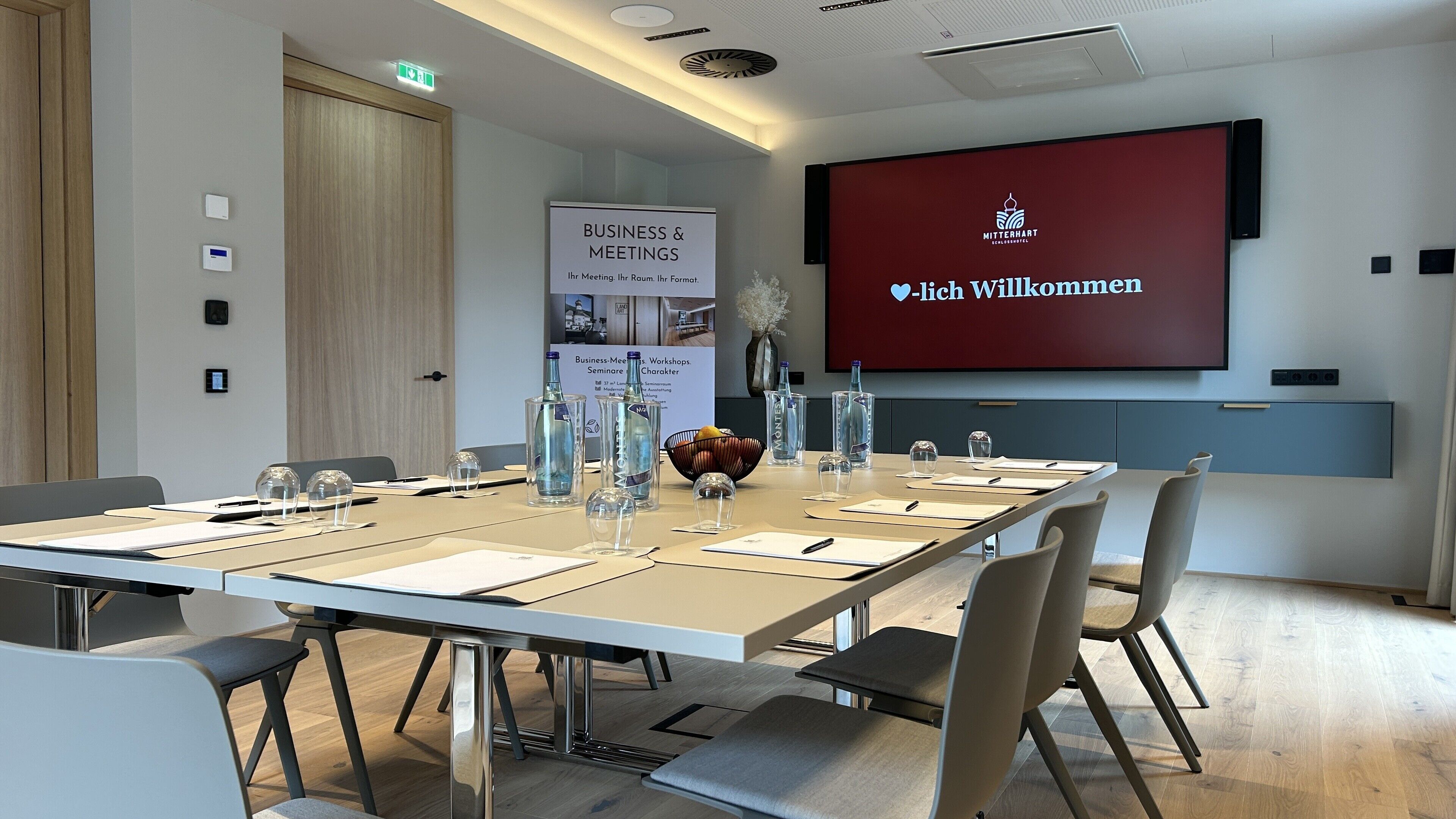 A conference room with a long table, chairs, a projector screen, and a banner.