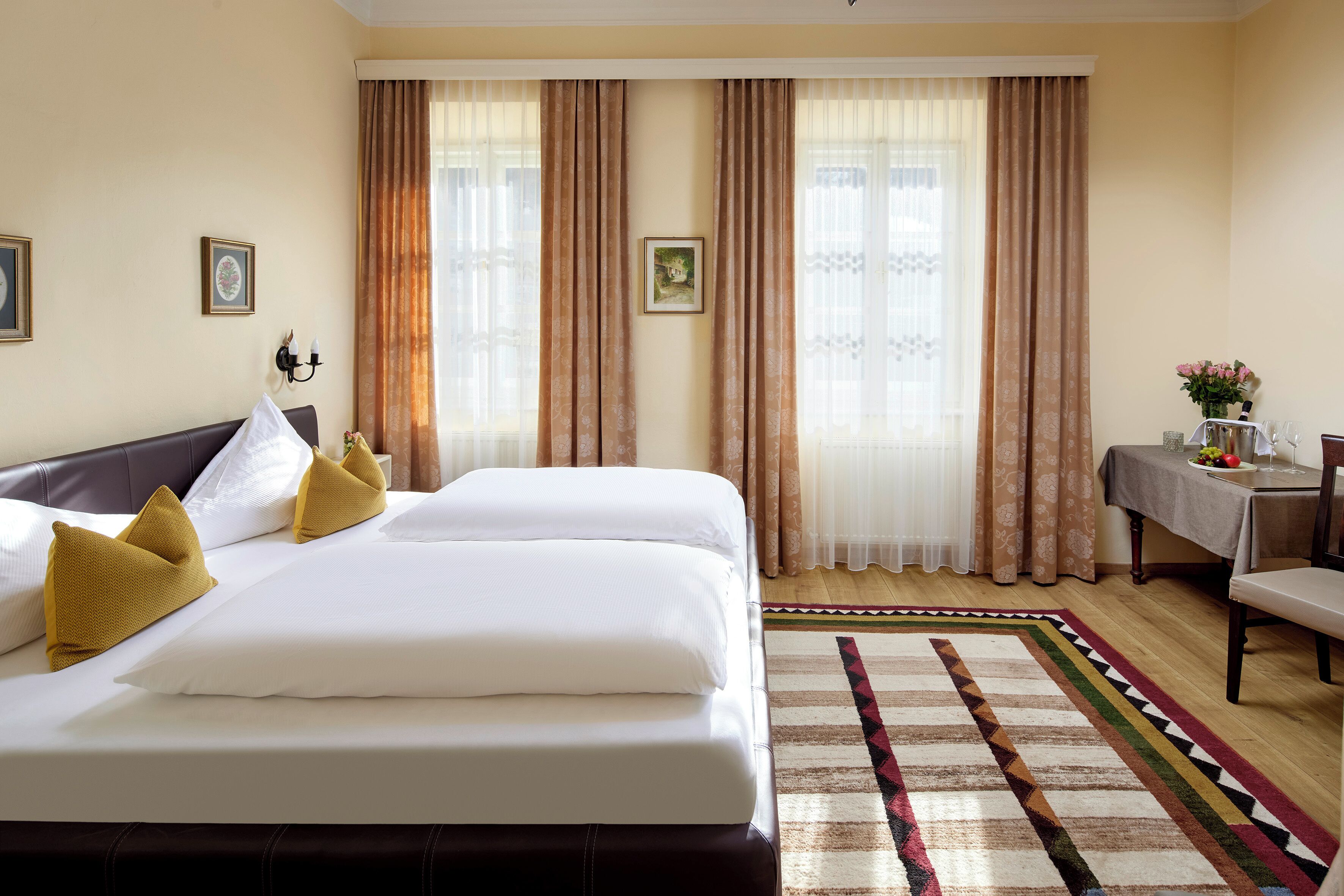 A hotel room with a large bed, a small table with a vase, and a chair.
