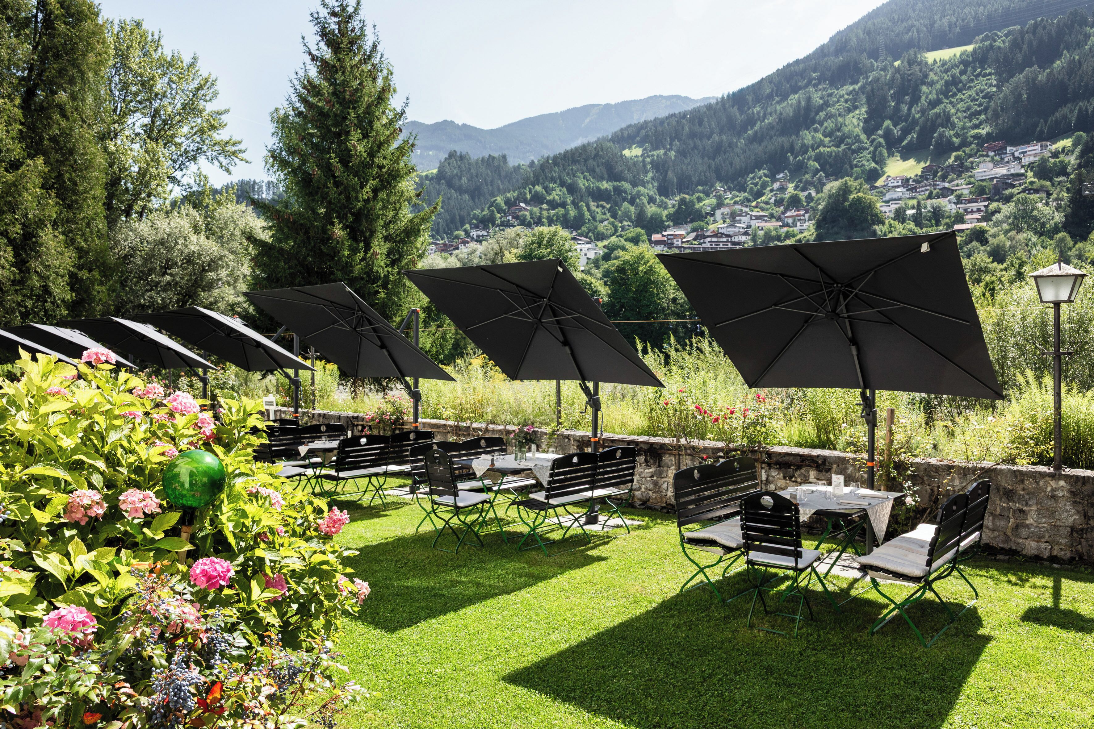 An outdoor seating area with tables and chairs, umbrellas, and a view of a mountainous landscape.