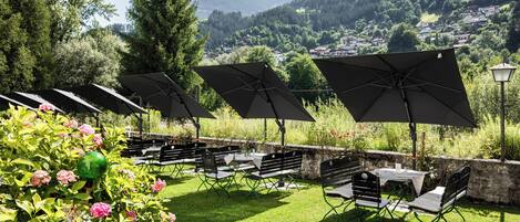 An outdoor seating area with tables and chairs, umbrellas, and a view of a mountainous landscape.