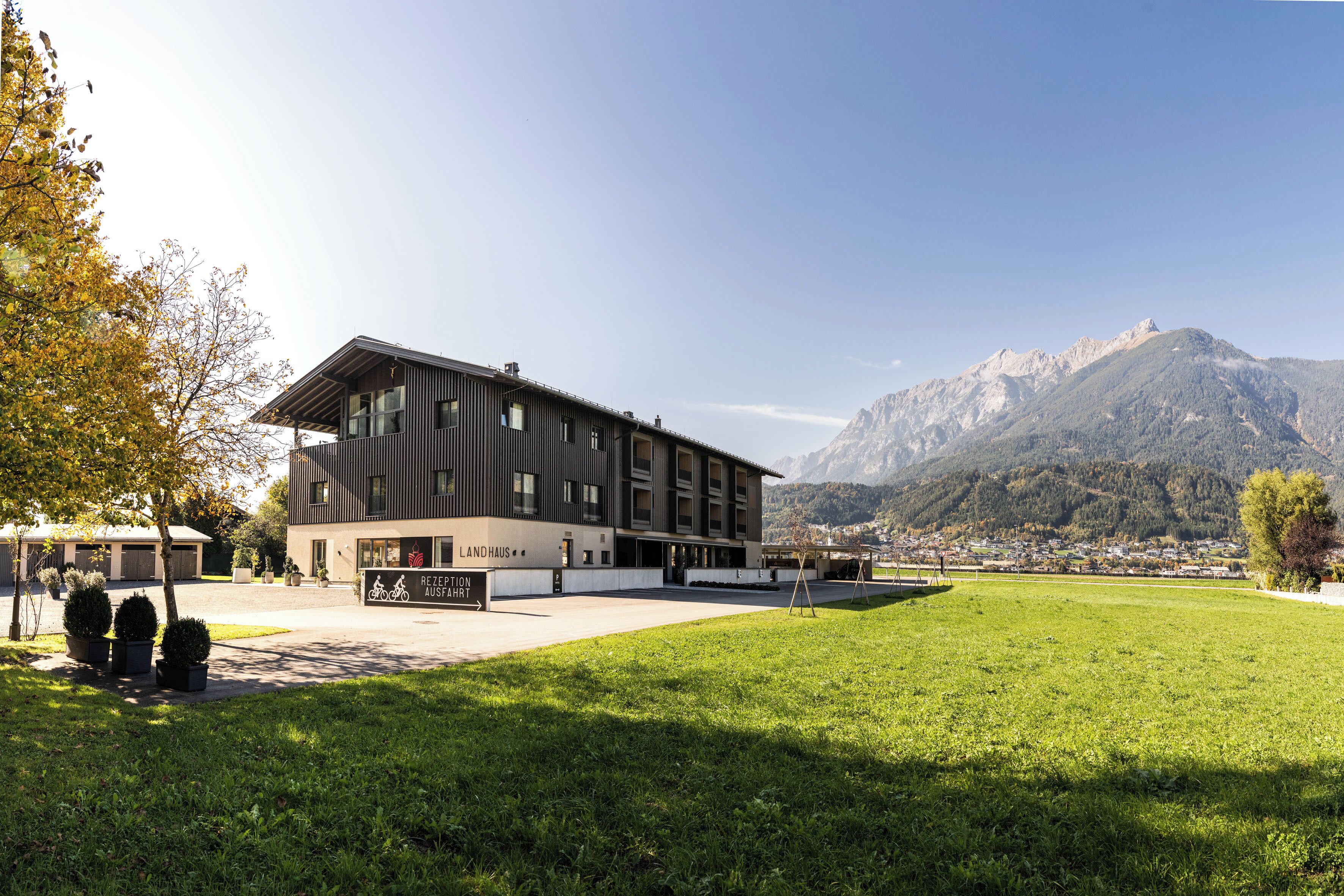 A modern building with a sign indicating a bicycle rental service, surrounded by a grassy area and mountains in the background.
