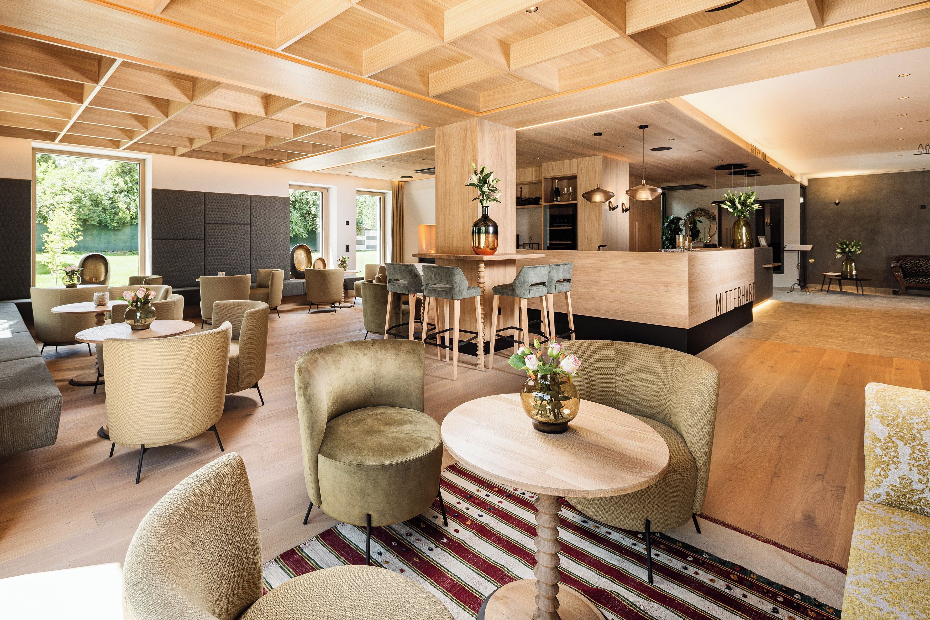 Un moderno hall de hotel con zona de bar, arreglos de asientos y un amplio ventanal con vistas a zonas verdes.
