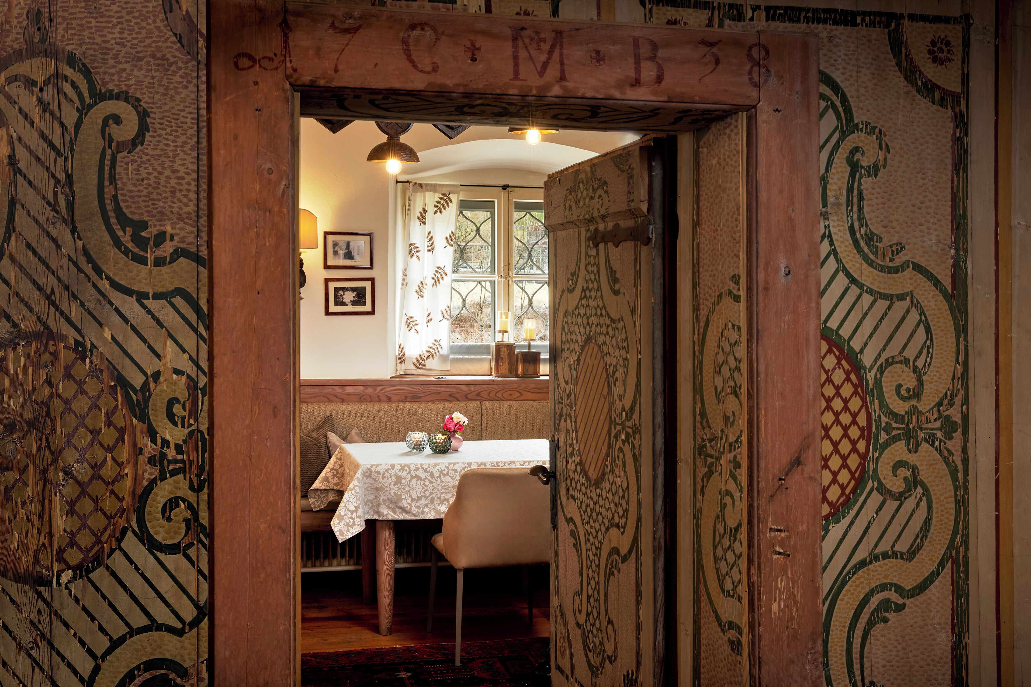 Una habitación con puerta de madera, una mesa con mantel blanco y una ventana con cortinas estampadas.