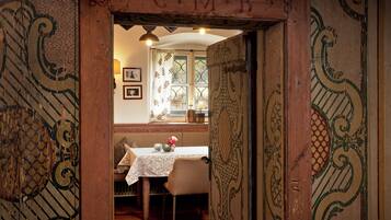 Una habitación con puerta de madera, una mesa con mantel blanco y una ventana con cortinas estampadas.