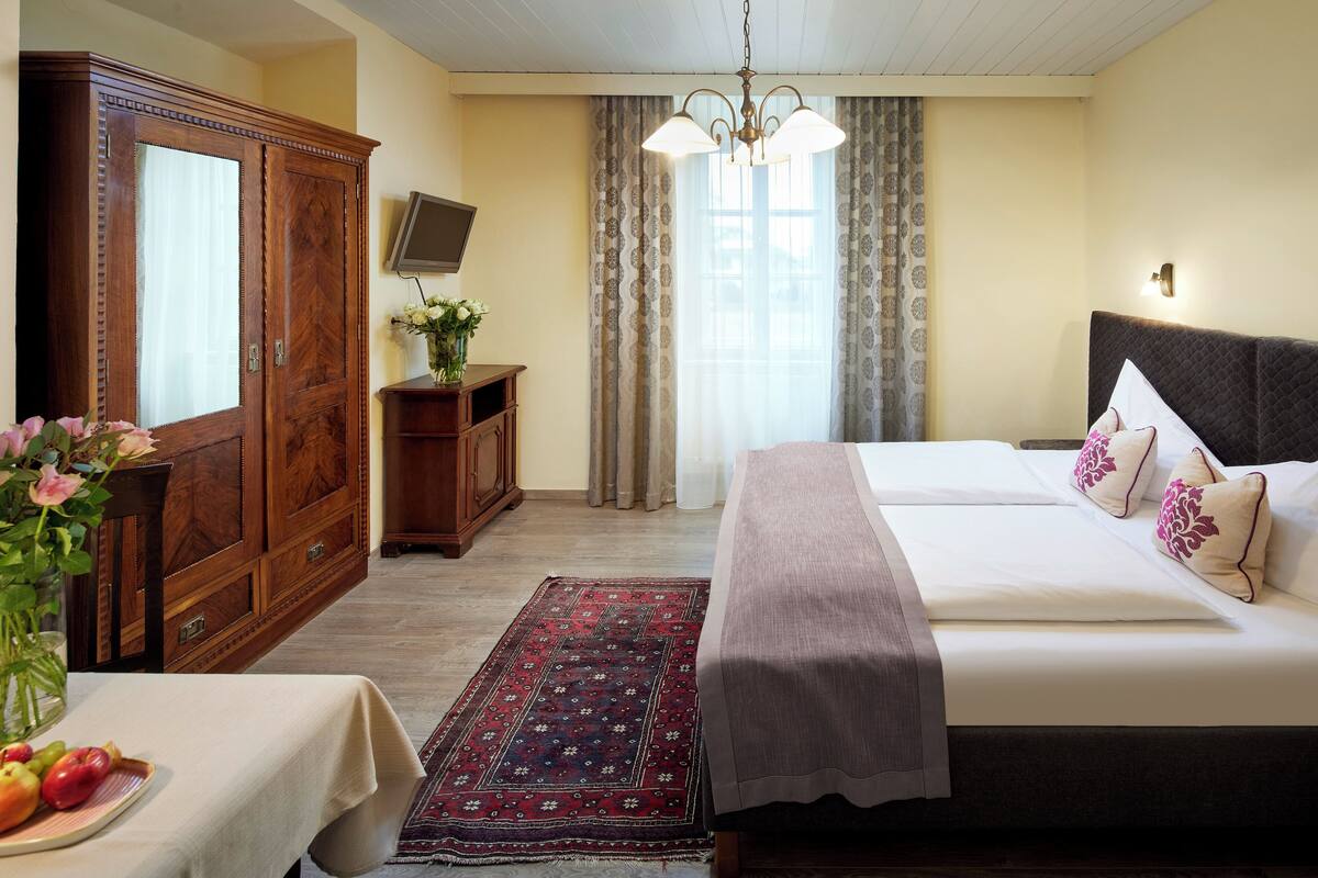 Une chambre d’hôtel avec un grand lit, une armoire en bois, une télévision et un tapis décoratif.