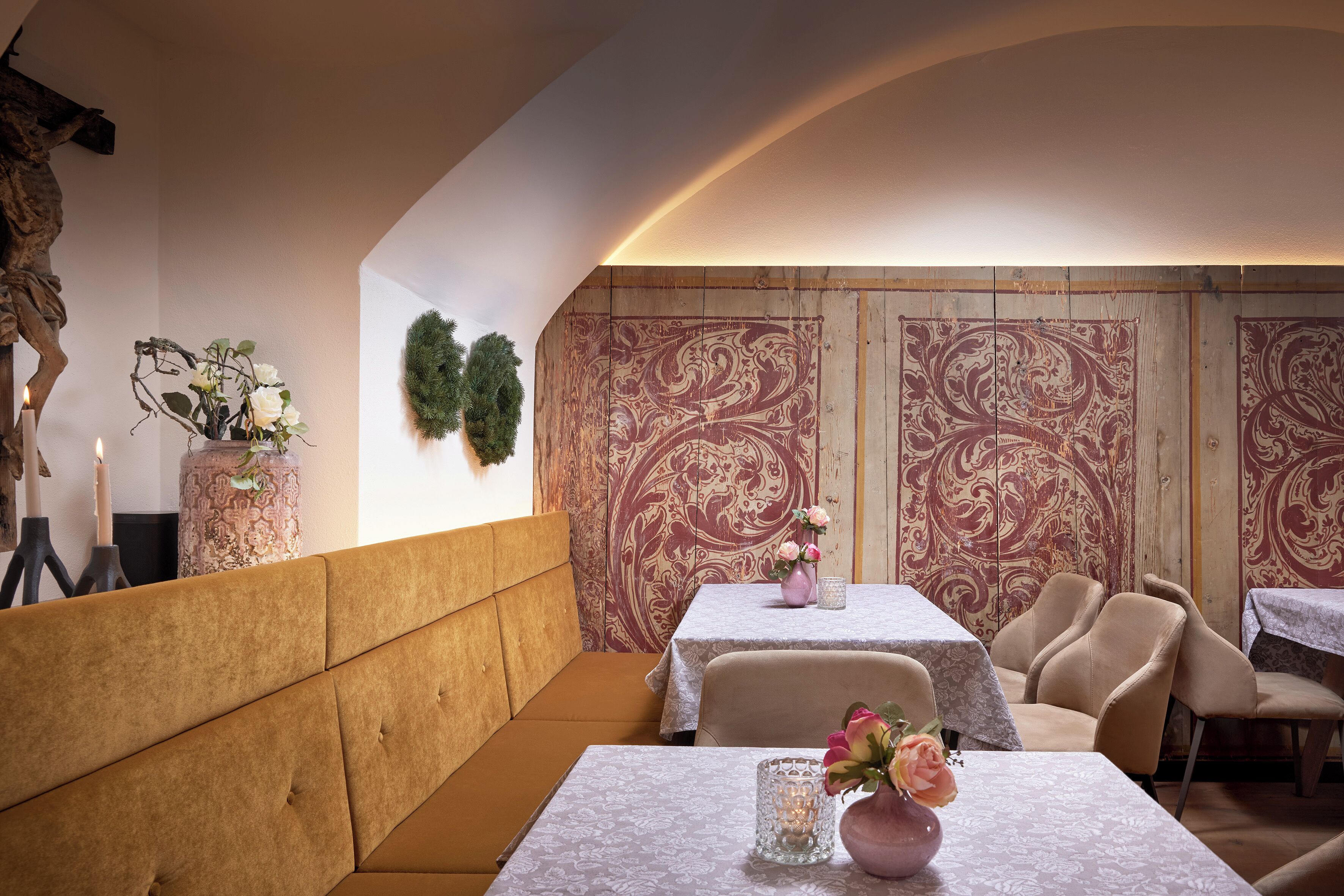 A restaurant interior with cushioned seating, tables with floral centerpieces, and patterned wallpaper.