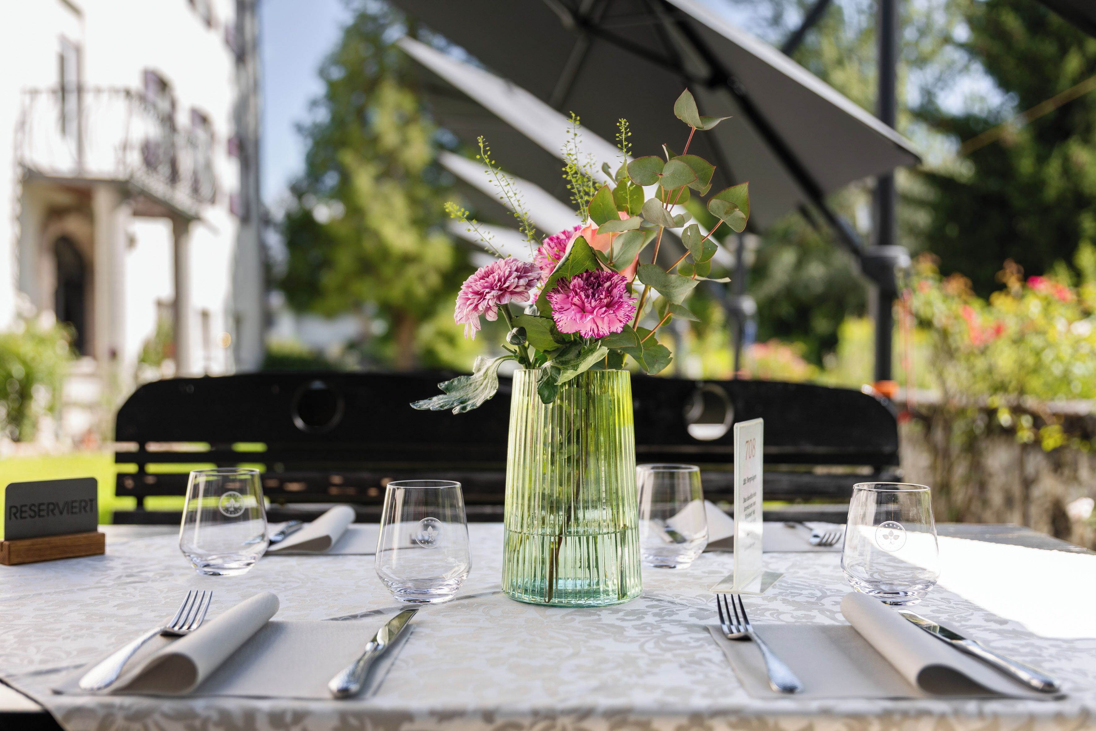 A table set for dining with a vase of flowers, a sign reading 'RESERVERT,' and a bench in the background.
