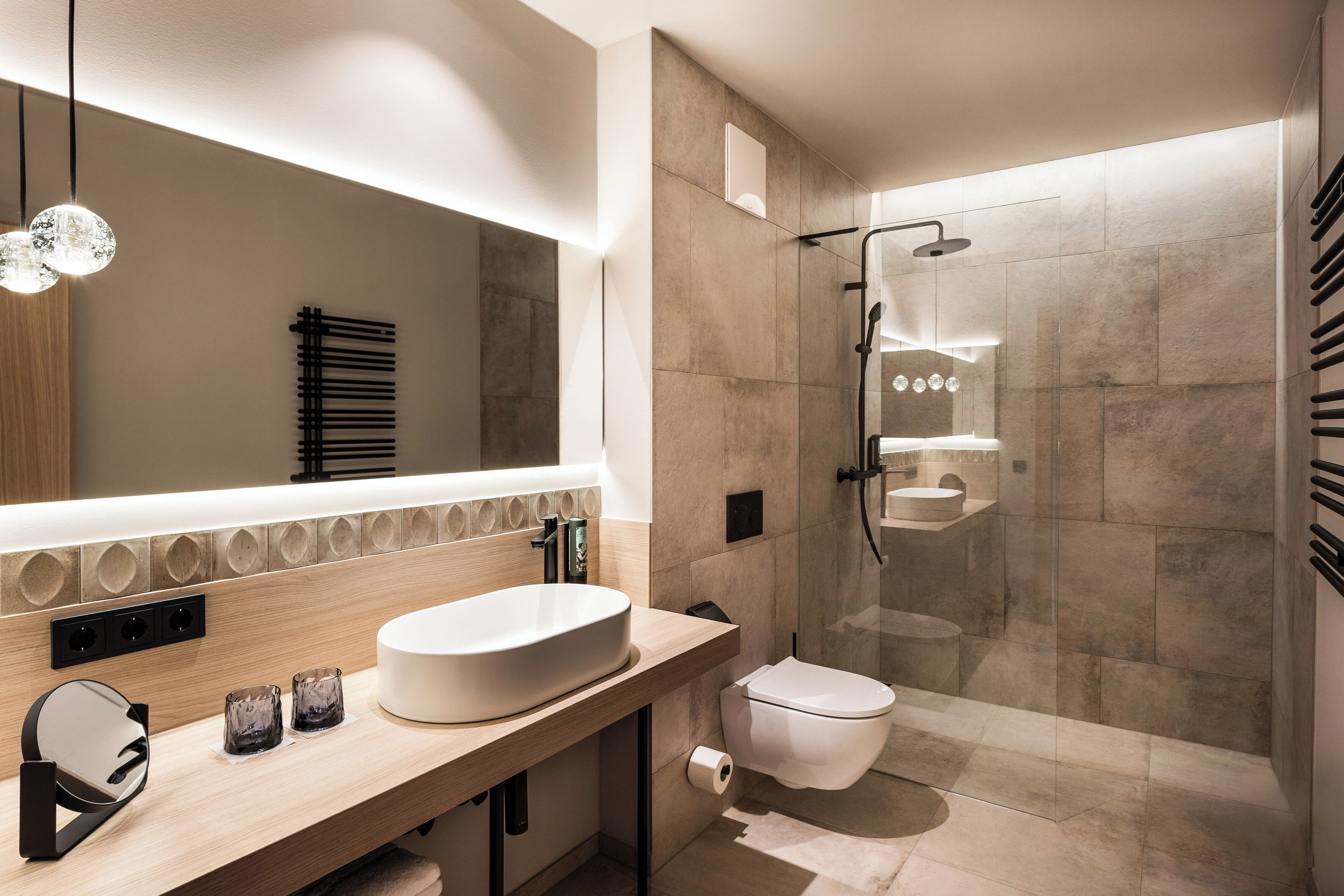 A modern bathroom with a large mirror, a sink, a toilet, and a glass-enclosed shower.