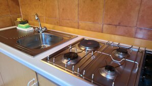Una cocina con un lavamanos de acero inoxidable, una estufa a gas con cuatro quemadores y un salpicadero de azulejos.