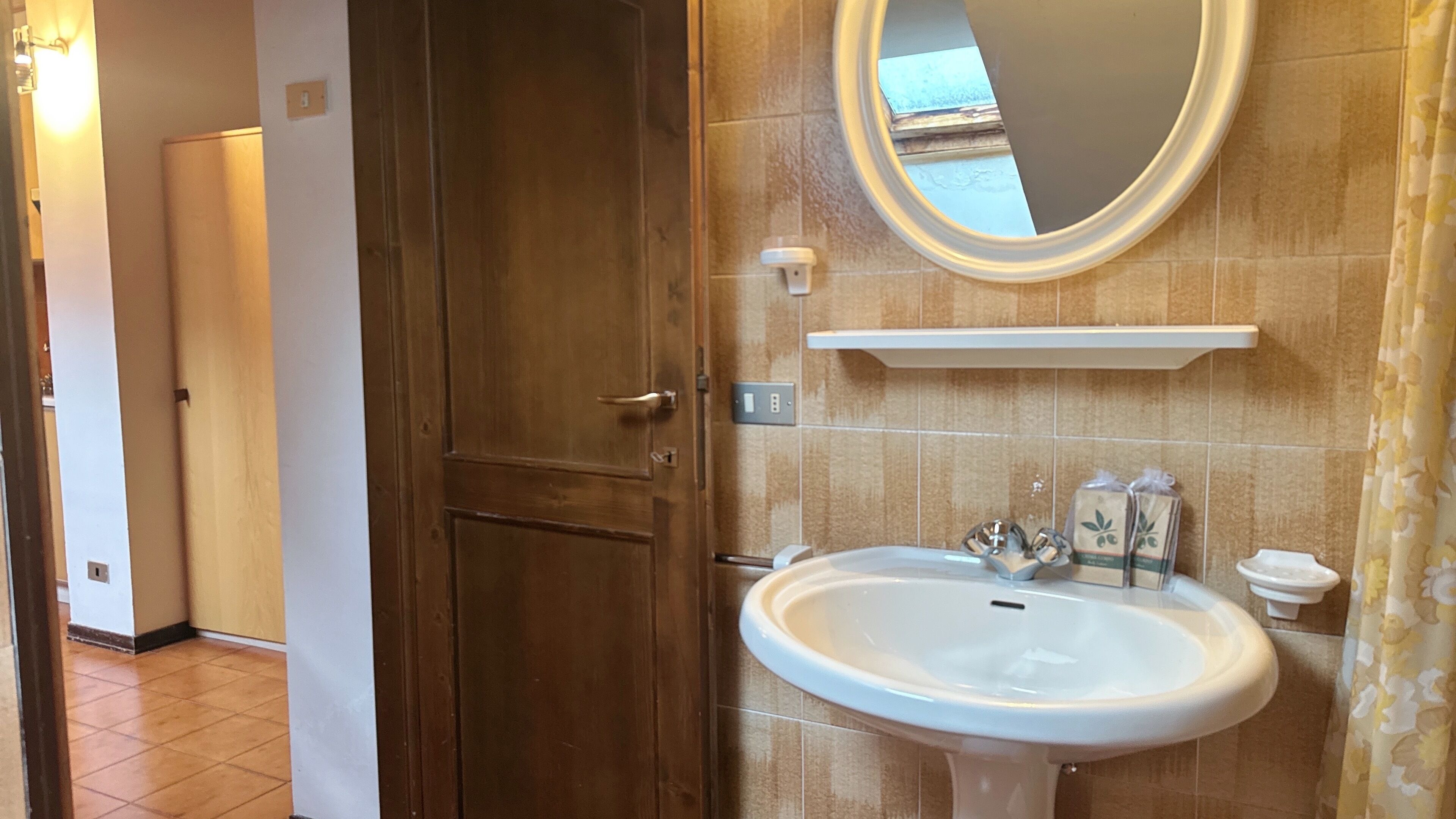 A bathroom with a wooden door, a white sink, a mirror, and a shower area.