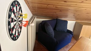 Una habitación con dardos en la pared, un sofá azul y techo de madera.