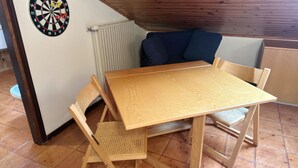 Un pequeño comedor con una mesa y sillas de madera, un dardo en la pared y un radiador.