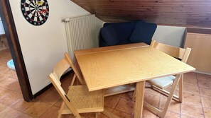 Pieni ruokailutila, jossa on puinen pöytä ja tuolit, seinällä on tikanheitotaulu ja huoneessa on patteri.