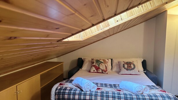 Un dormitorio con techo inclinado, una cama con ropa de cama escocesa y dos almohadones decorativos.