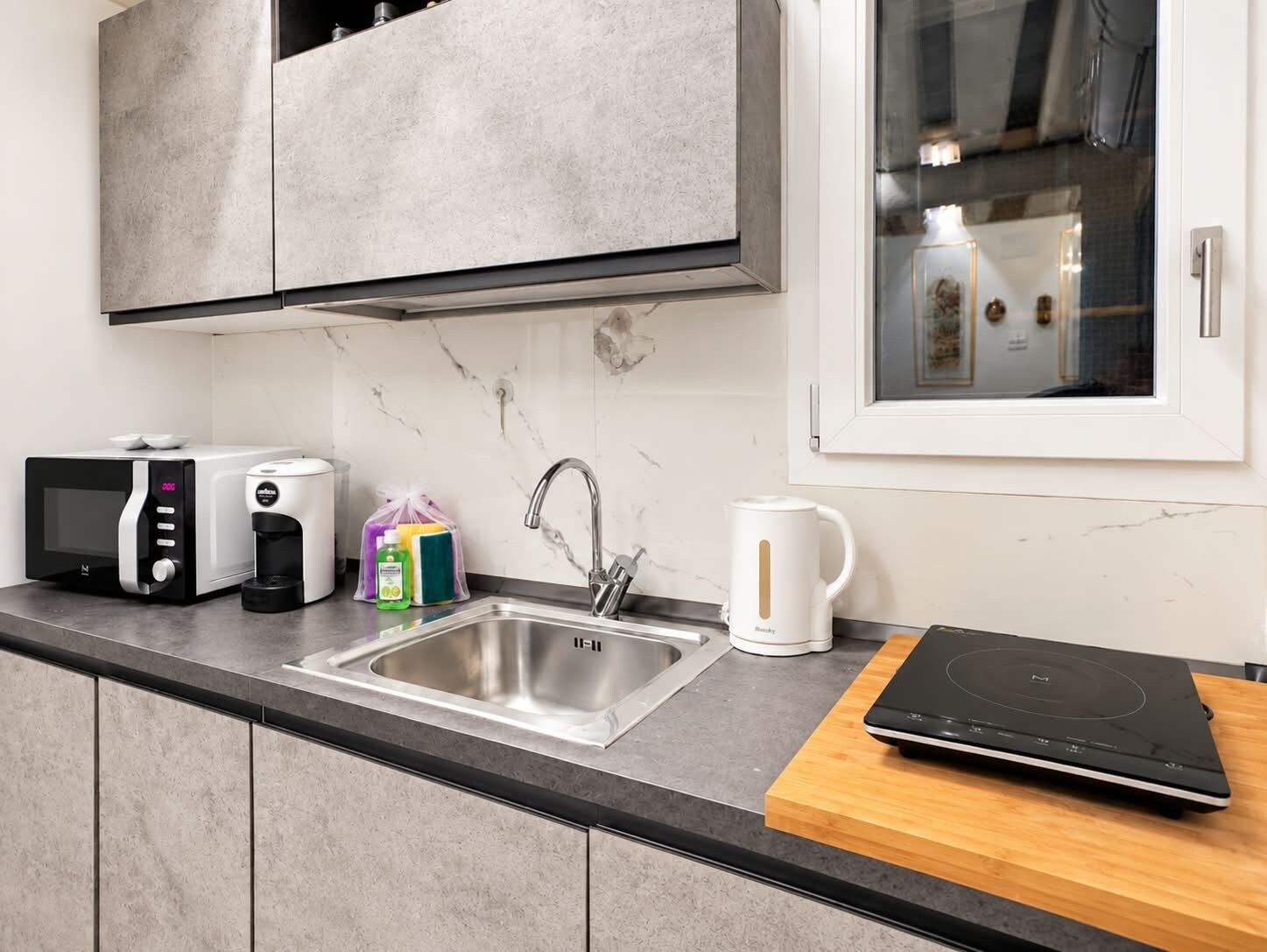 Cocina moderna con microondas integrado, cafetera, lavaplatos y ventana con vista al interior.