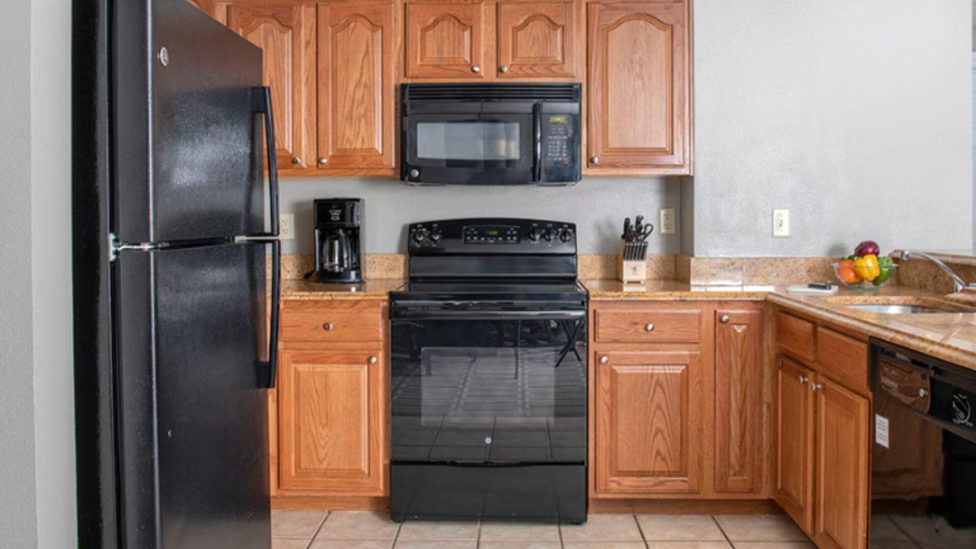 Une cuisine avec des meubles de rangement en bois, un réfrigérateur noir, un four à micro-ondes et une cuisinière.