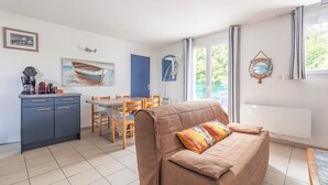Ein Wohnzimmer mit Sofa, Esstisch, Stühlen, einer Küchenzeile mit Schränken und einem großen Fenster mit Vorhängen.