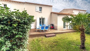 Ein Haus mit Terrasse, einem Tisch mit Stühlen, einer Tür und einem kleinen Garten.