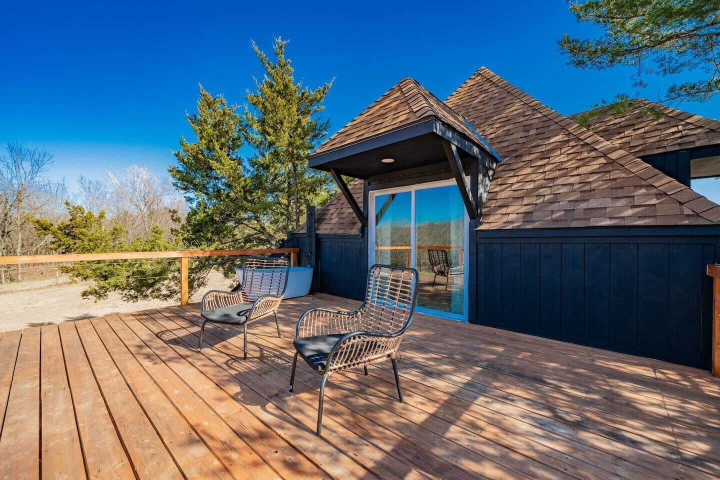 Eine Holzterrasse mit zwei Korbstühlen, einer überdachten Veranda und Blick auf die umliegende Landschaft.