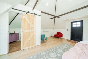 A spacious room with a wooden sliding door leading to a kitchen, a red chair, and a black door.