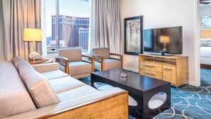 Quarto de hotel com sofá, cadeiras, televisão e escrivaninha.
