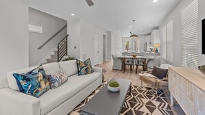 A modern living room with a sofa, coffee table, and a dining area with a table and chairs. - Design-Forward 3BR: King Suite, Pet-Friendly Fenced Yard, Office, Near Greenway (Raleigh)