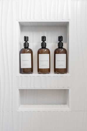 Three bottles of shampoo, conditioner, and body wash in a white shelf. - Design-Forward 3BR: King Suite, Pet-Friendly Fenced Yard, Office, Near Greenway (Raleigh)