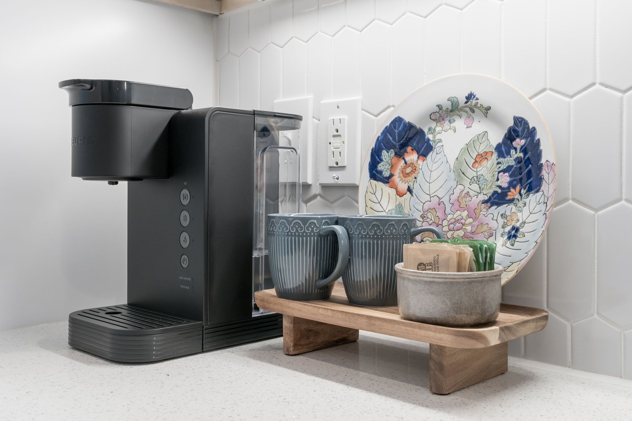 A modern kitchen with a coffee maker, a decorative plate, and a tray with cups and a bowl.