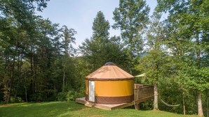 Eine Jurte mit Holzterrasse und Hängematte, umgeben von einem Wald.
