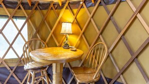 Ein runder Holztisch mit einer Lampe und zwei Stühlen in einem Raum mit einer Gitterwand und gelbem Stoff.