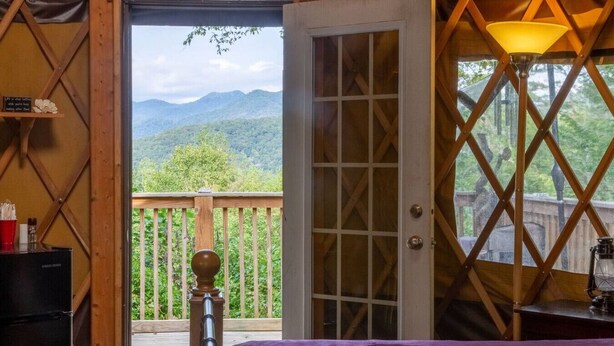 Ein Zimmer mit einer Holzdiele, einer violetten Bettdecke, einer Holztür und Bergblick.