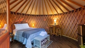 A cozy yurt with a bed, a small table with chairs, and a lamp. - Holly Hideaway | Cozy Yurt | Pet Friendly & Trails (Cullowhee)