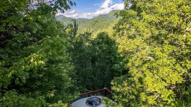 A circular observation deck with a glass dome, surrounded by dense green foliage and a mountainous backdrop. - Holly Hideaway | Cozy Yurt | Pet Friendly & Trails (Cullowhee)