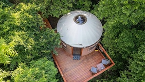 A dome-shaped structure with a wooden deck and seating area, surrounded by dense greenery. - Holly Hideaway | Cozy Yurt | Pet Friendly & Trails (Cullowhee)