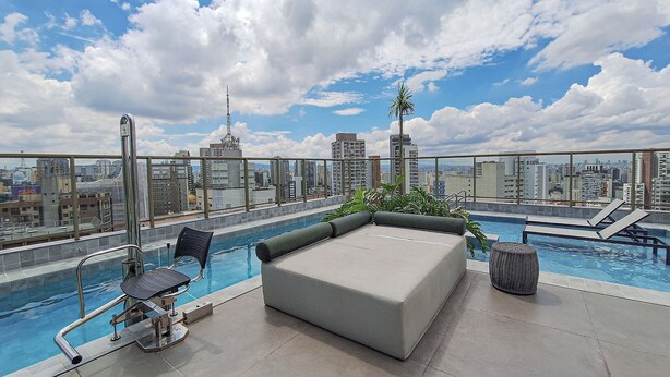 Una piscina en la azotea con vistas a la ciudad, sillones de descanso y una pequeña mesa.